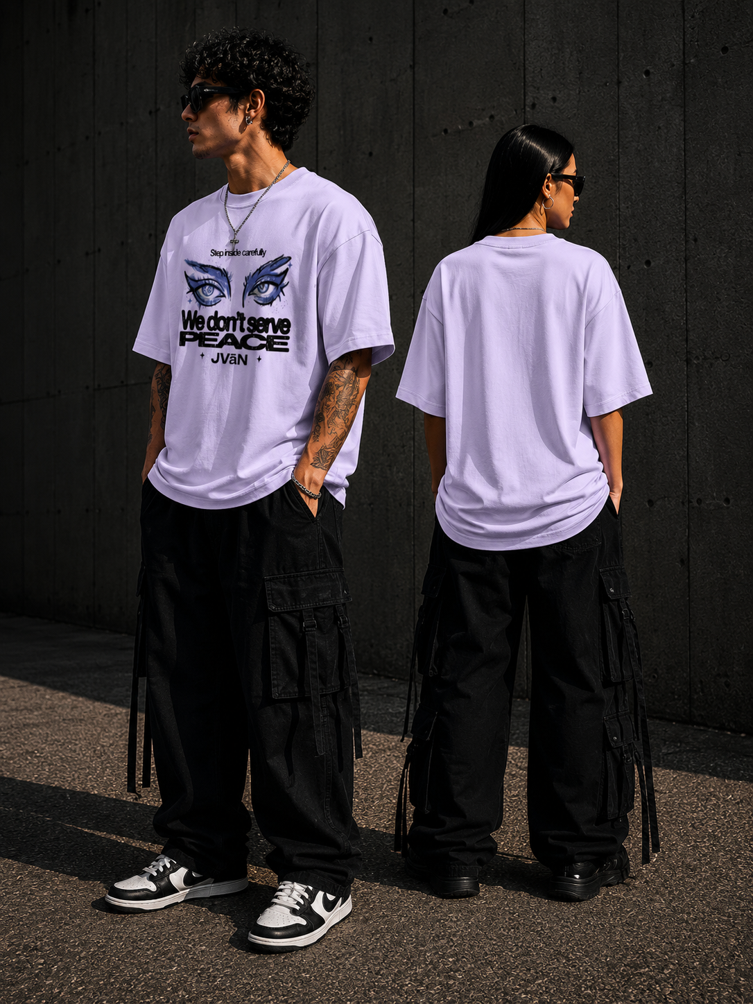 Two people wearing matching white t-shirts with a graphic design, standing against a dark wall.